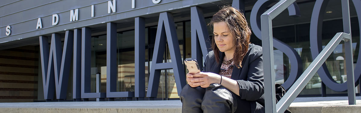 ysu student using smart phone near entrance of williamson hall 