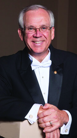 Portrait of guest conductor, Joseph Hermann. He is posing in a formal black and white tuxedo.