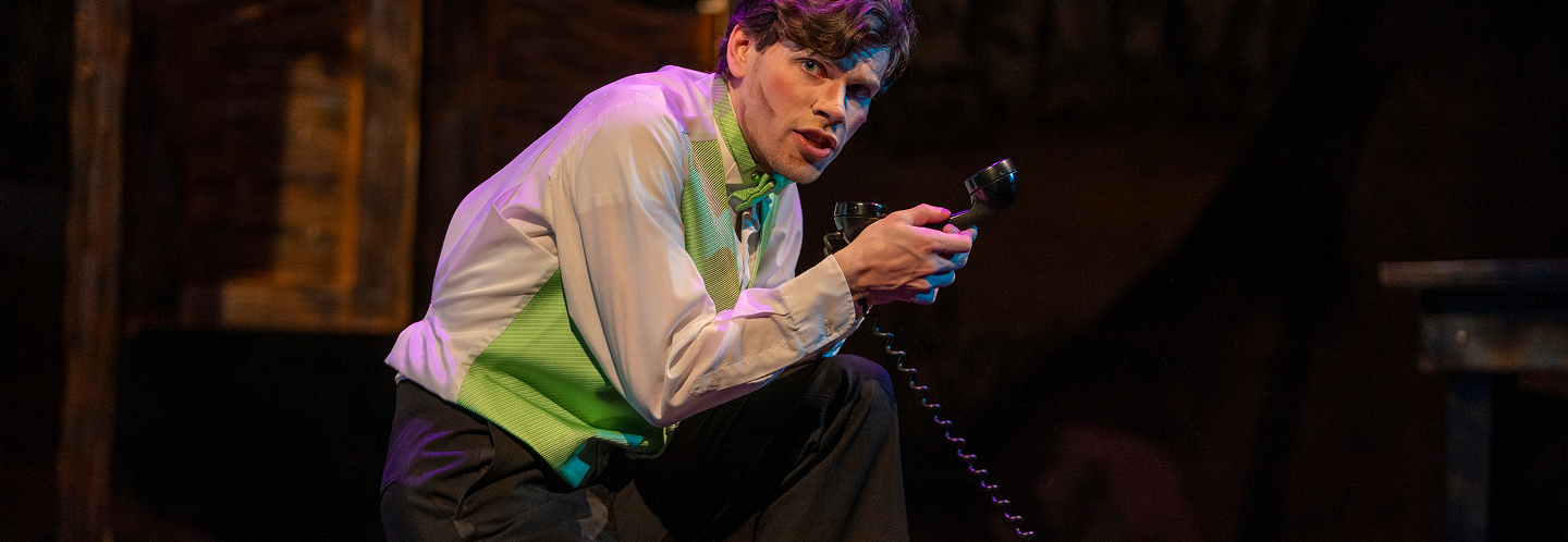 Actor addressing audience while holding an old telephone receiver