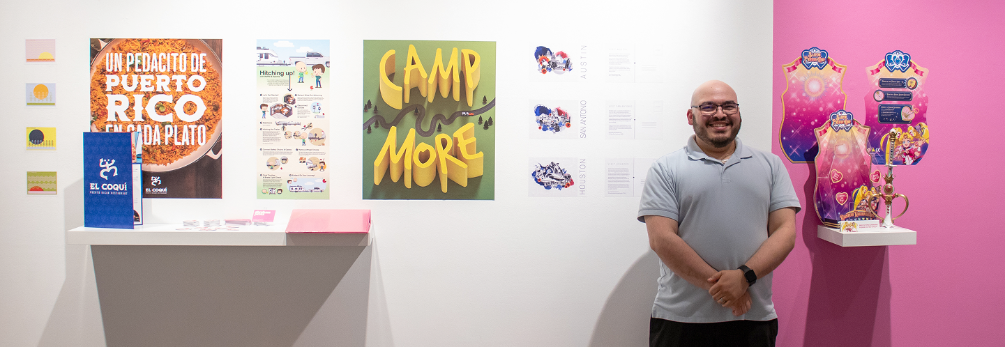 BFA graduate Abe Perez standing next to his graphic design work at the BFA graduation exhibition