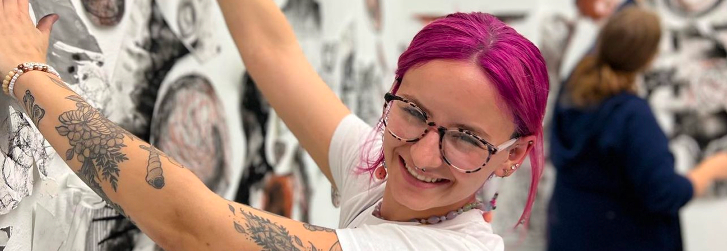 Female art student pausing to smile while installing a large drawing for an exhibition in the McDonough Museum of Art. 