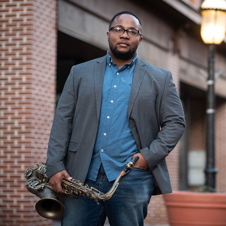 Photo of Stephen Harvey holding saxophone in front of brick wall