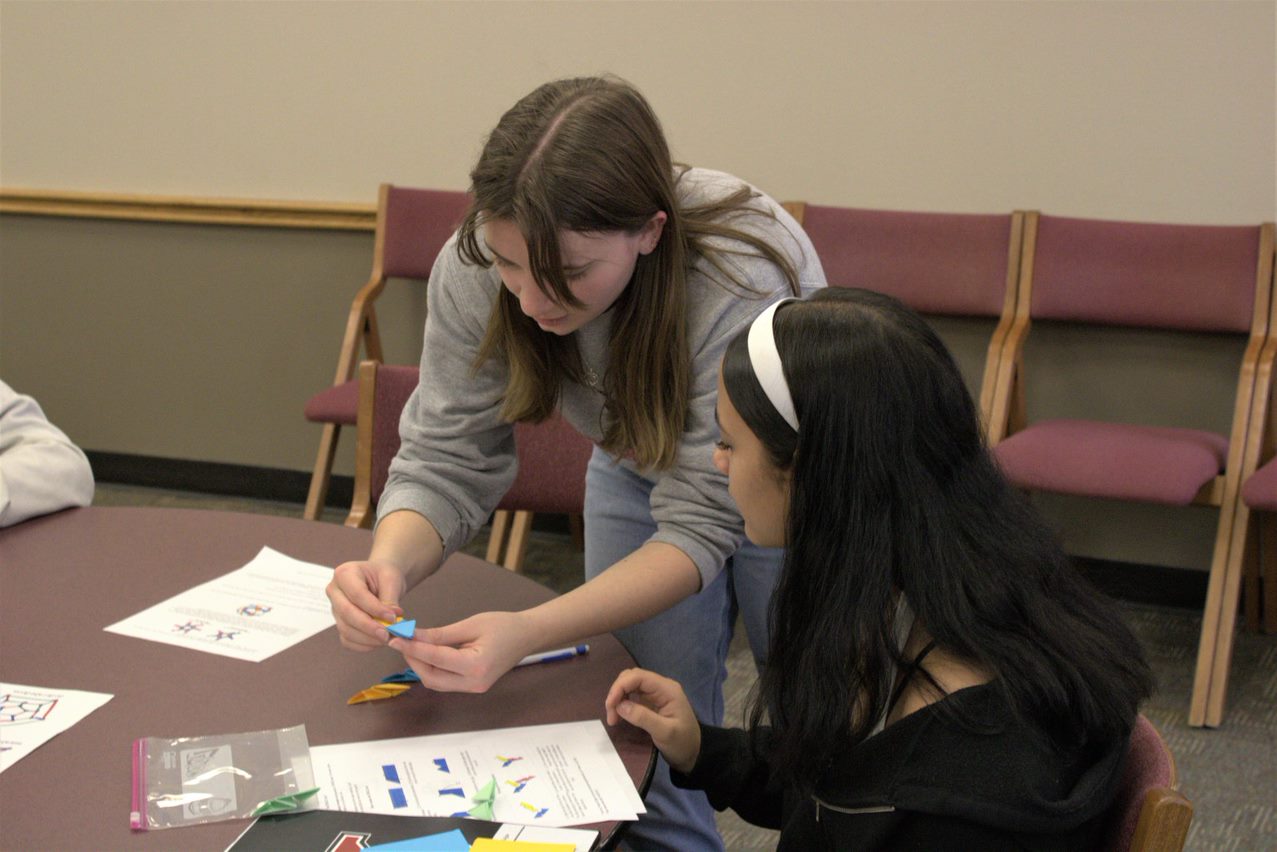 A YSU Student assists a mathfest participant in origami folding